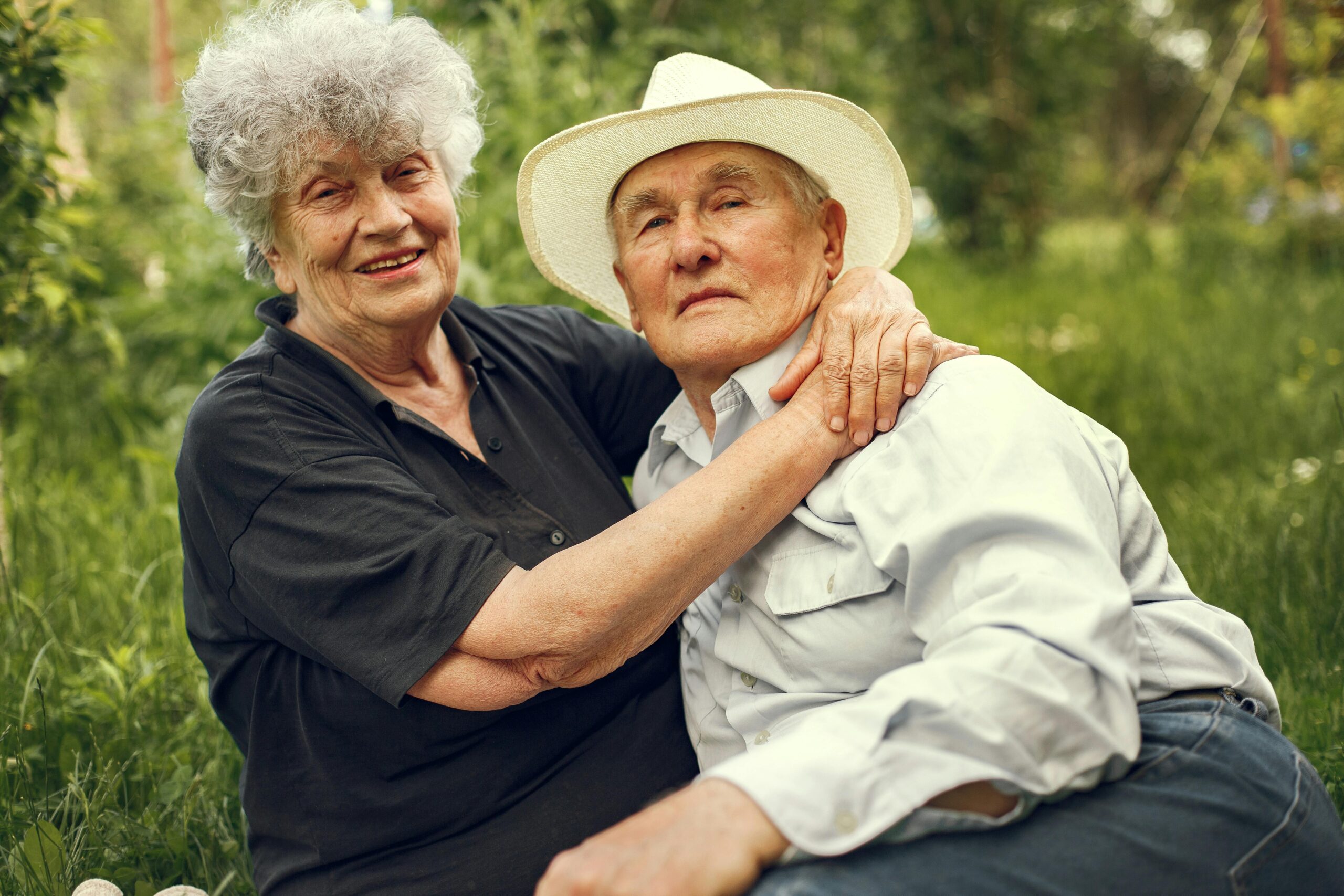 Happy elderly couple sitting together in a lush garden embracing and smiling.